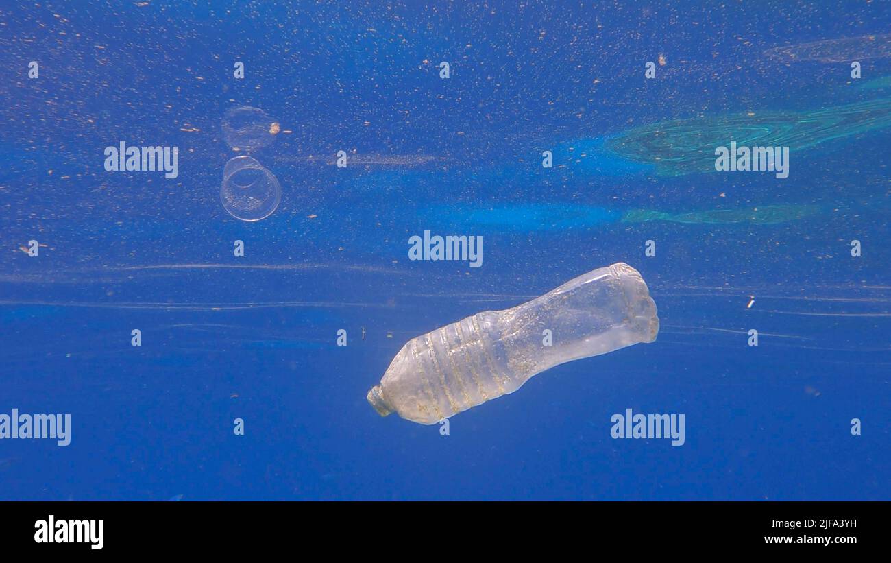 Plastic pollution, plastic bottle and cup in blue water. Discarded