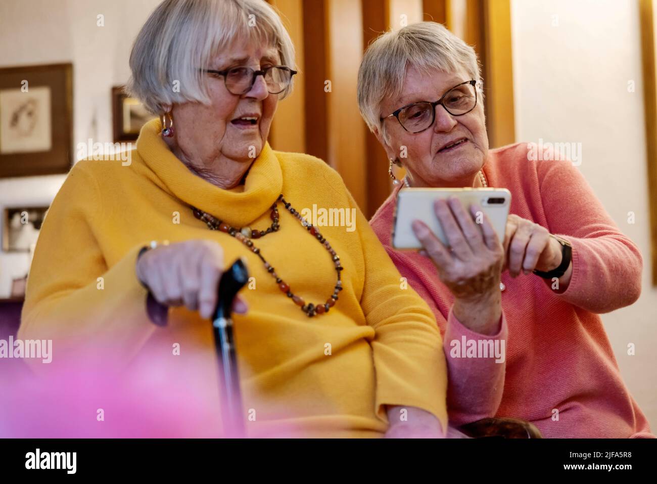 Two senior citizens, sisters, looking at a smartphone at home, Bocholt, North Rhine-Westphalia, Germany Stock Photo