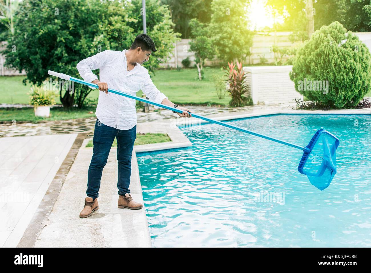 A man cleaning pool with leaf skimmer. Man cleaning the pool with the