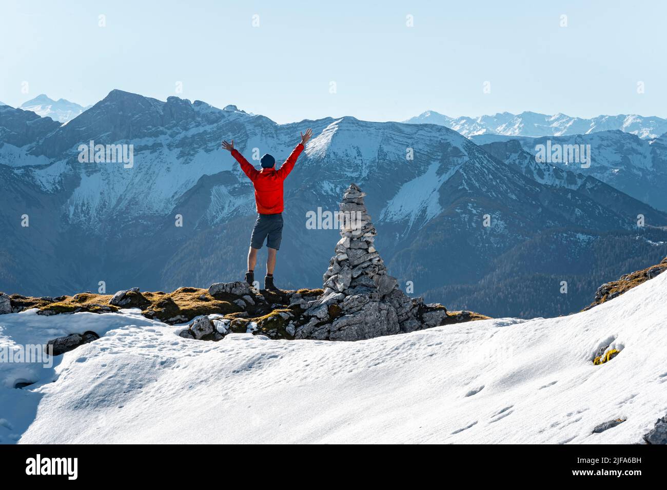 Mountaineer stretching his arms in the air, next to a cairn, in front of snow-covered mountains of the Rofan, hiking trail to Guffert with first Stock Photo