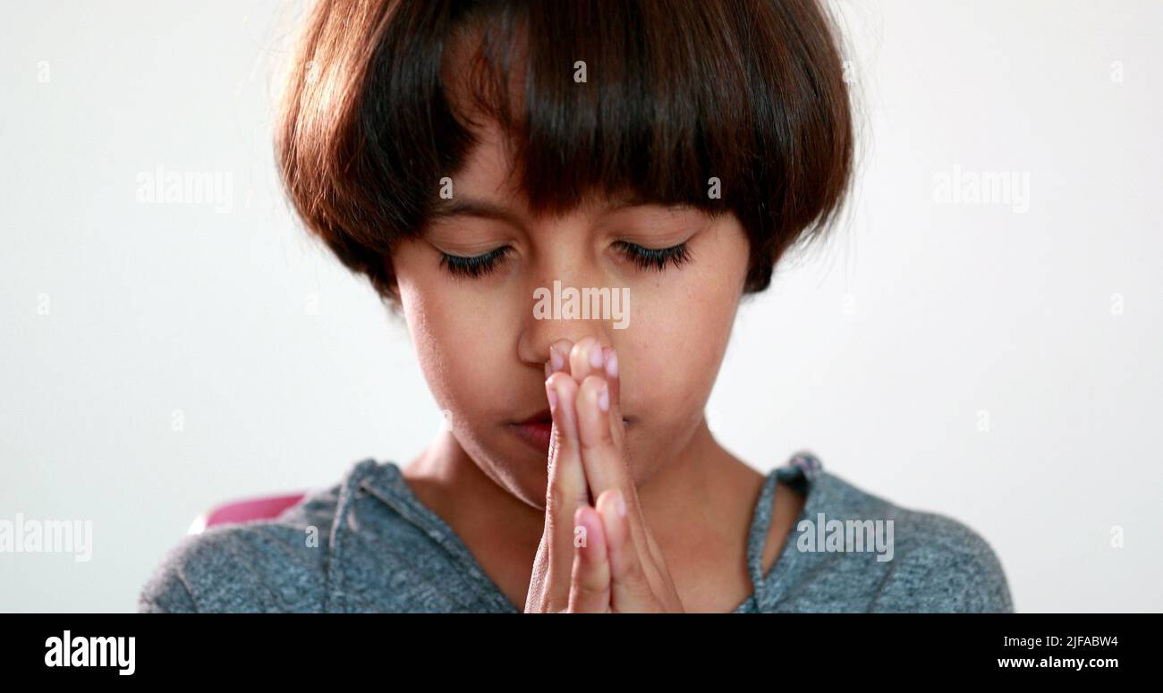 Child boy praying to God with hands held together with closed eyes