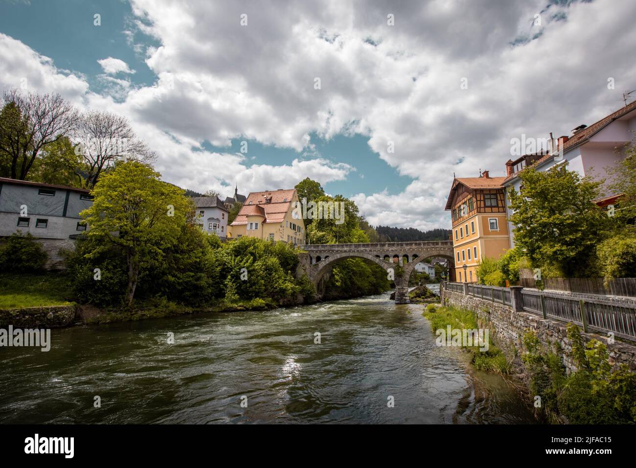 Mura or Mur river flowing through Murau city centre, in central part of austria on a cloudy but sunny day. Stone bridge and classical buildings are se Stock Photo