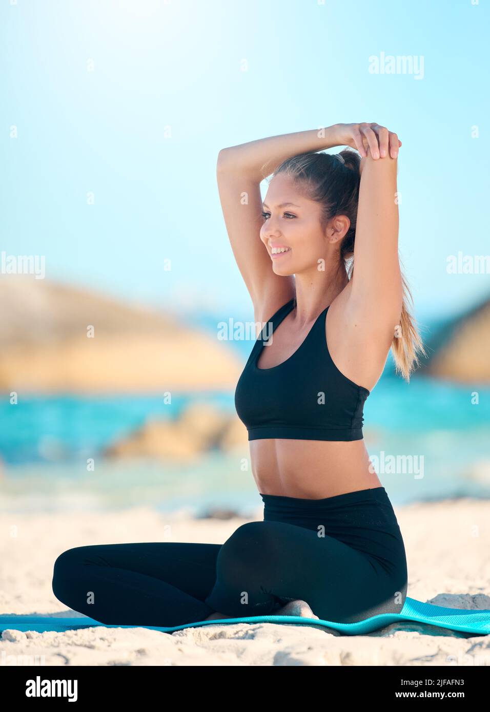 Beautiful woman practising yoga exercise on the beach. Young female athlete stretching while working out outside. Finding inner peace, balance and Stock Photo