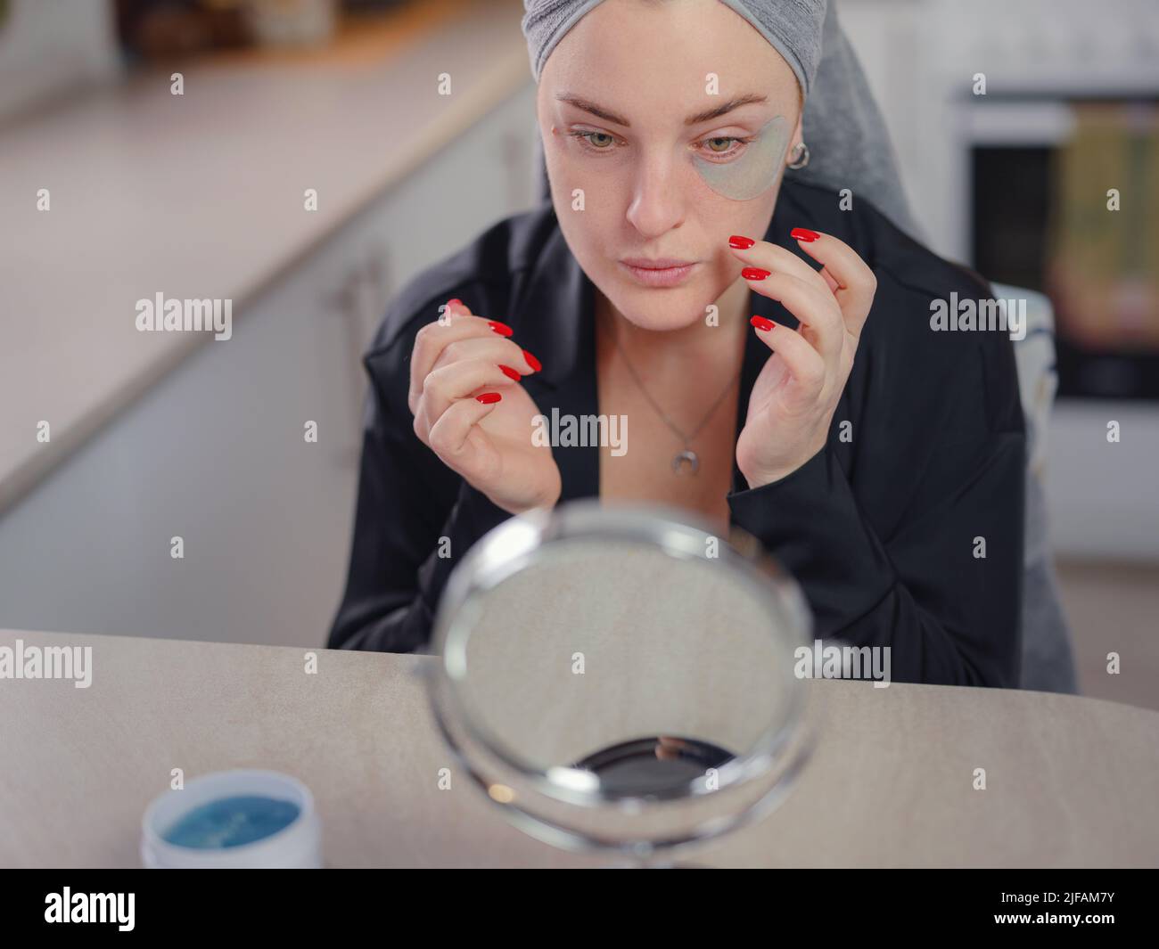 Patches for eyes. Attractive woman in kitchen with towel on her head