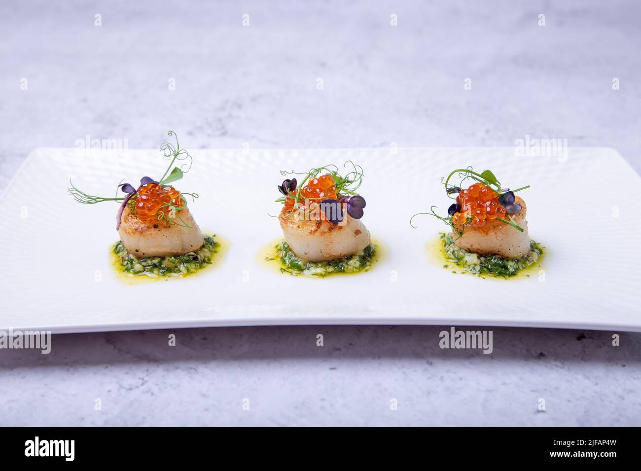 Scallops with caviar, microgreens and green sauce on a white plate. Close-up. Stock Photo