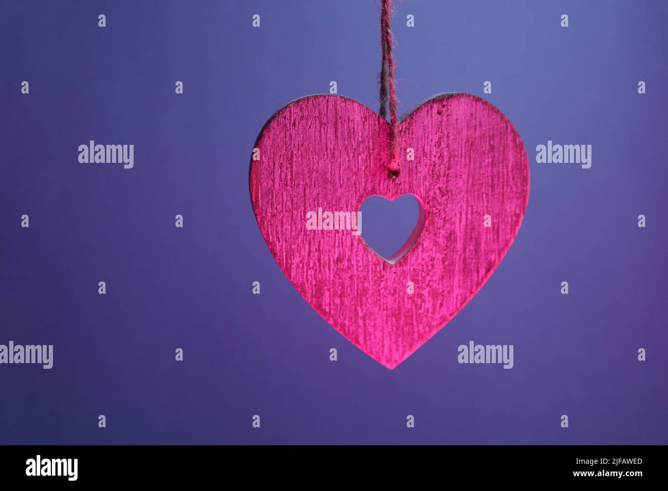 Pink wooden heart suspended by string against a dark blue-purple background Stock Photo