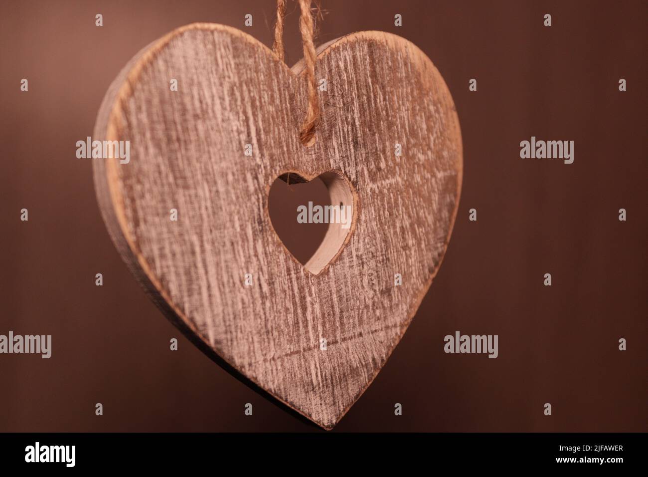 Grey wooden heart suspended by string against a dark background Stock Photo