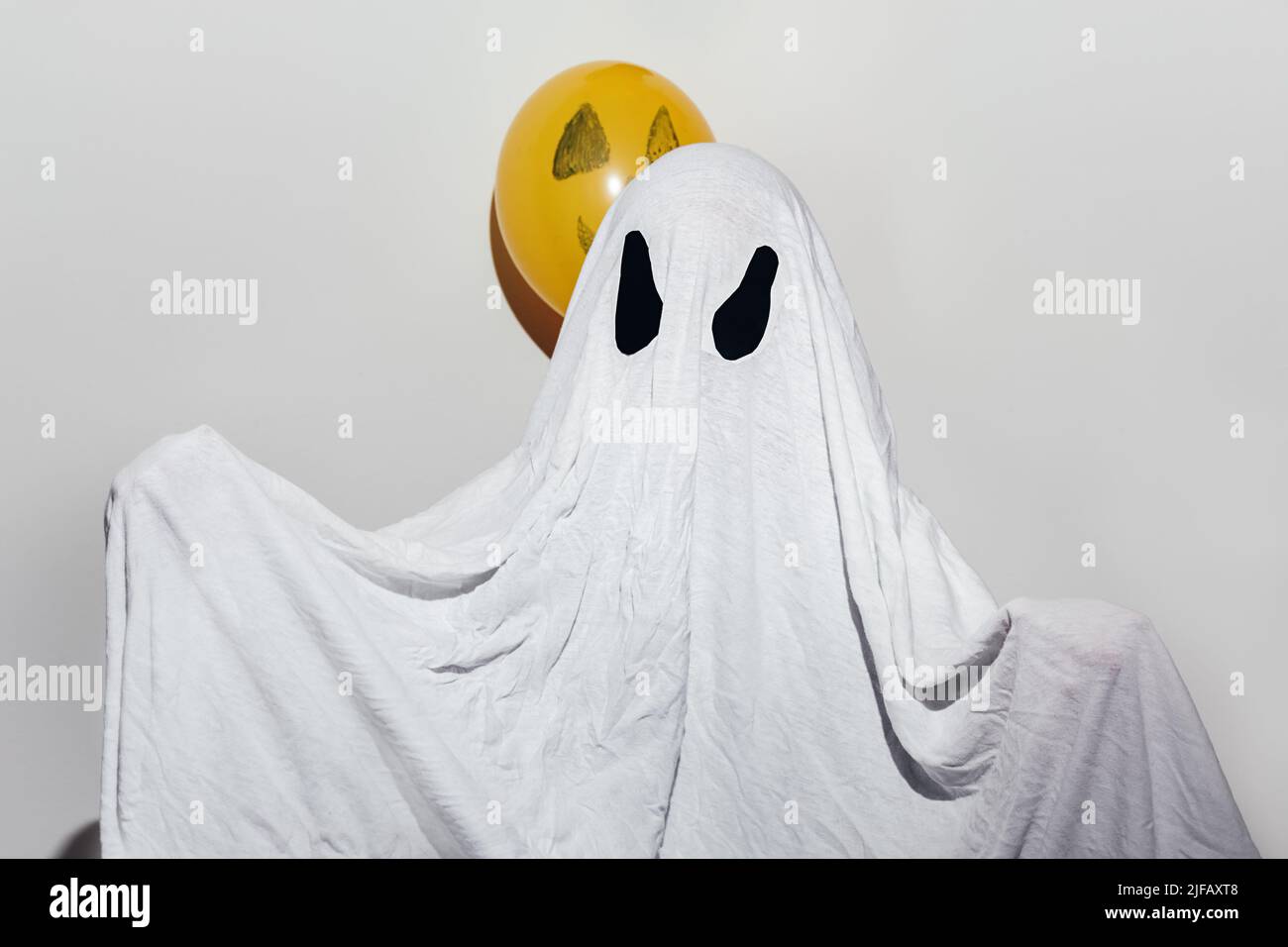Happy Halloween. A child in a white homemade ghost costume and painted orange balls. Festive design, party concept. All Saints Day celebration. Stock Photo