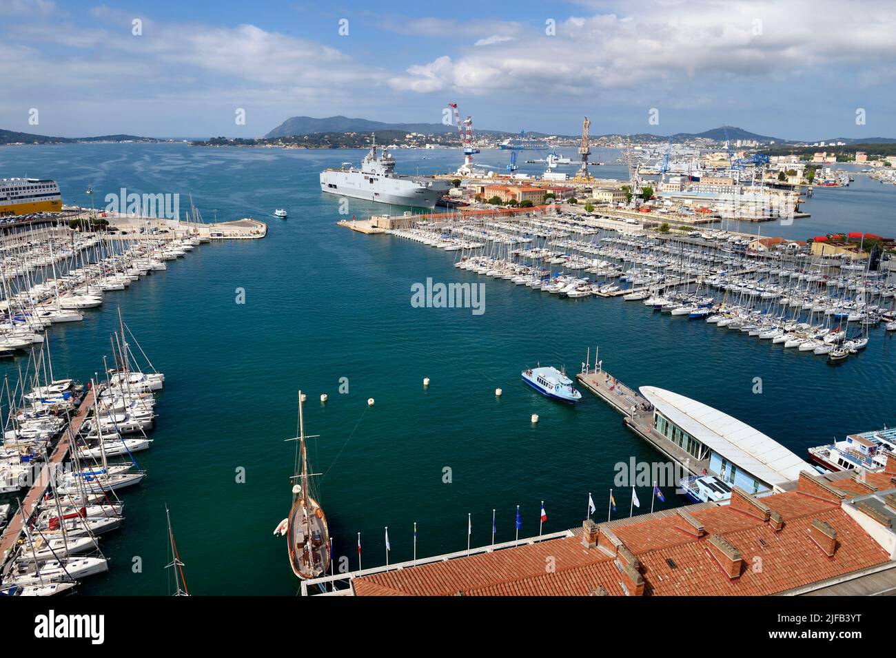 France, Var, Toulon, water bus pier of the Maritime Station quay Kronstadt on the civil port, the Mistral (L9013) amphibious helicopter carrier of the French Navy in the background in the naval base (Arsenal) Stock Photo