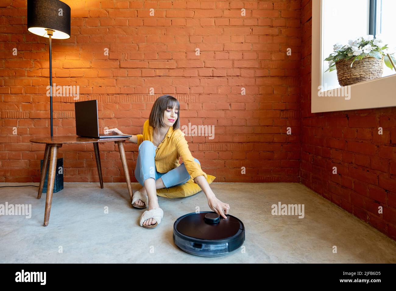 Woman work on laptop while robotic vacuum cleaner cleaning floor at ...