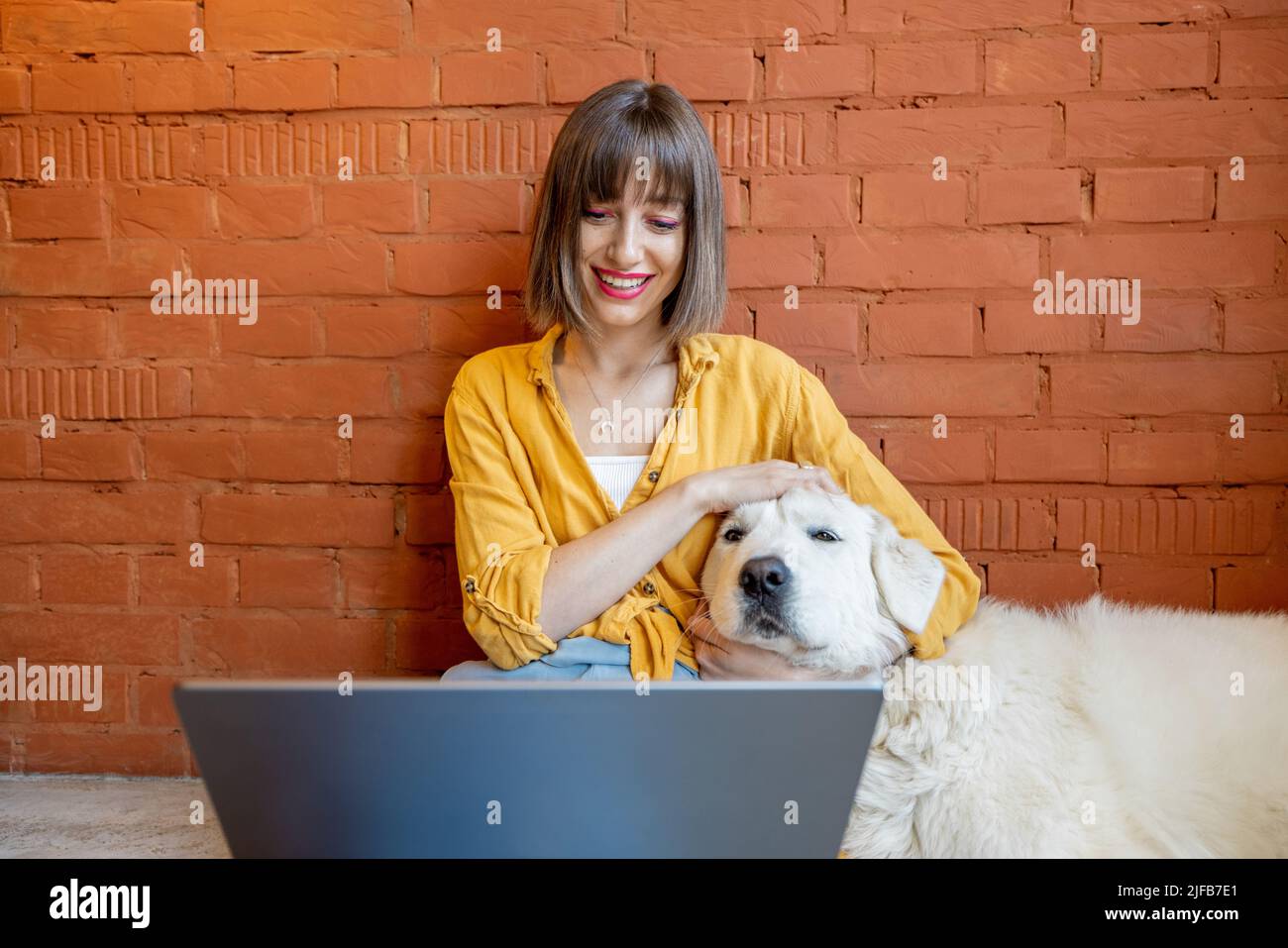 Woman working on laptop computer while sitting with her dog at home ...