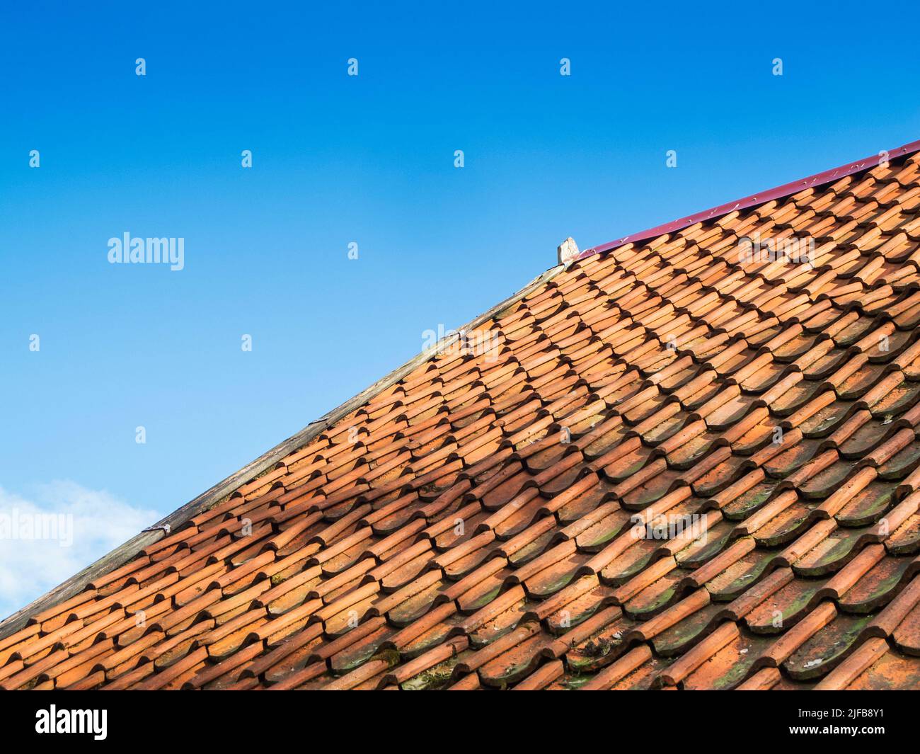 Oblique lateral partial view of a pitched roof covered with shingles in bottom view in front of a cloudless sky in sunshine. Stock Photo
