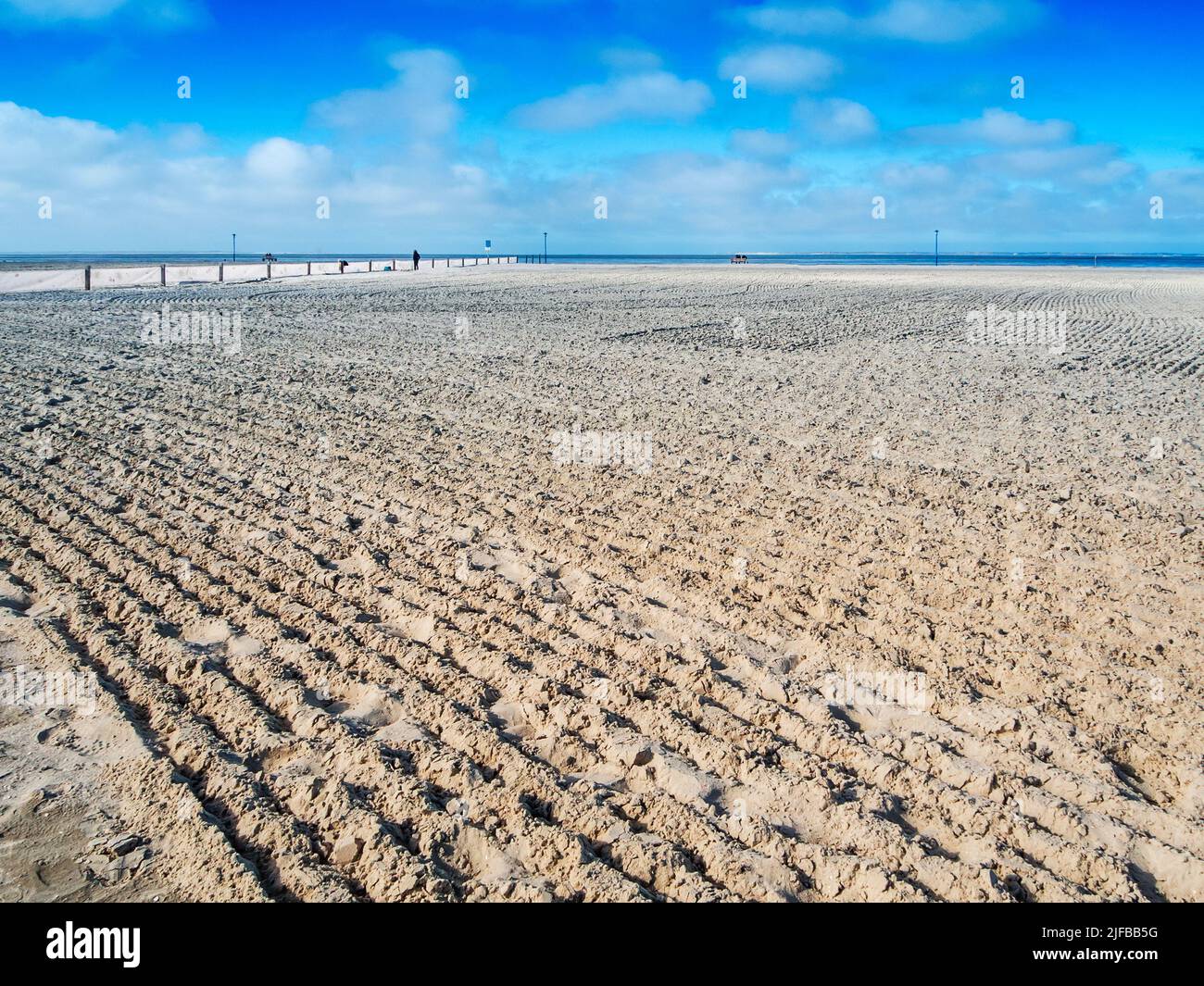 Landscape view of the German North Sea beach near Neuharlingersiel with a freshly smoothed empty sunbathing beach in front of a blue sky. Stock Photo