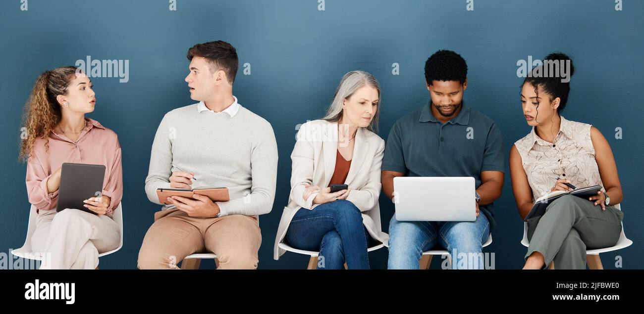 Group of diverse serious businesspeople sitting on chairs in a row in an office together. Five business professionals sitting and talking using Stock Photo
