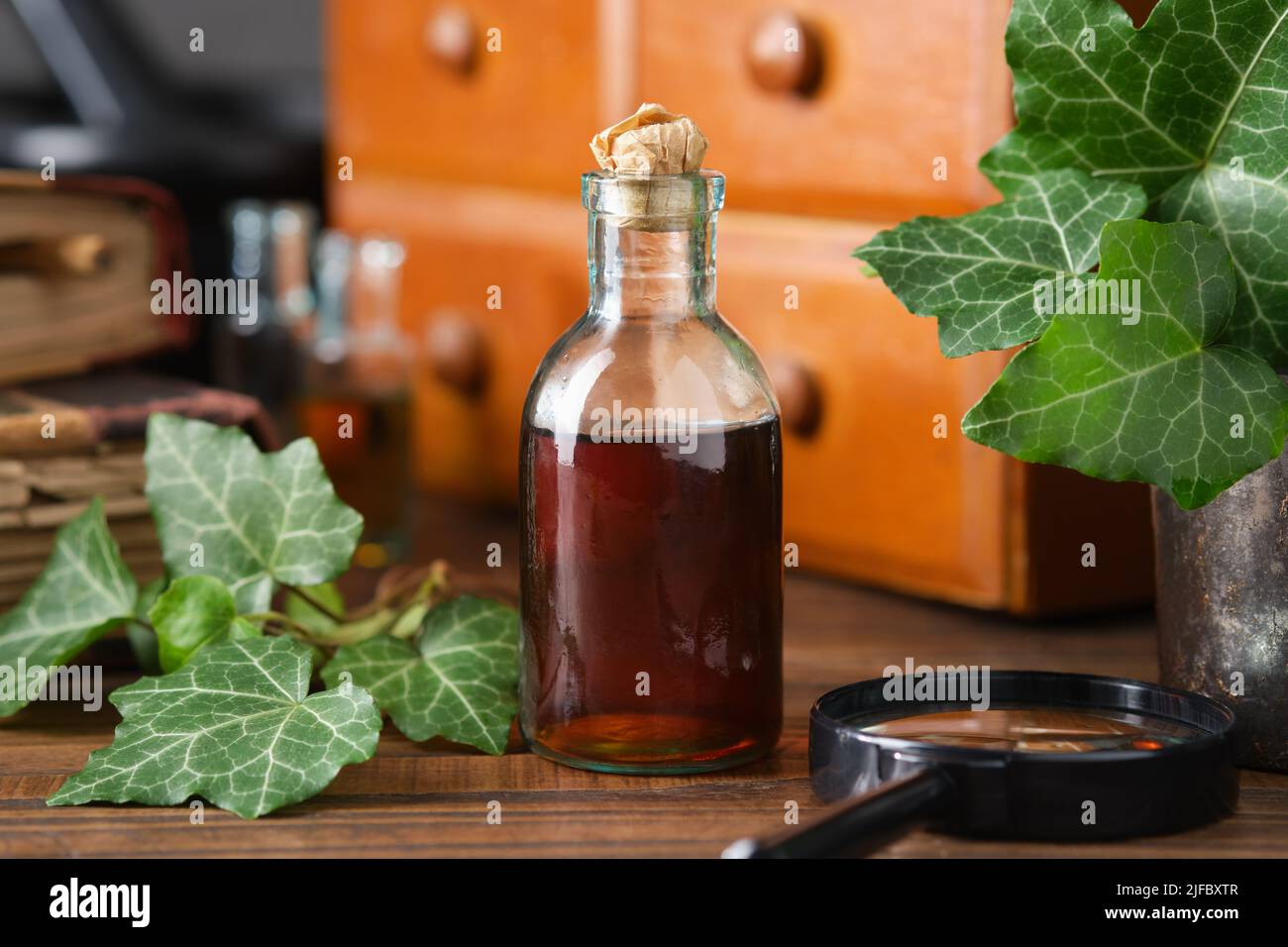 Bottle of ivy leaf syrup or cough tincture. Ivy leaves extract bottle and wooden medicine cabinet with apothecary remedies, old books on background. A Stock Photo