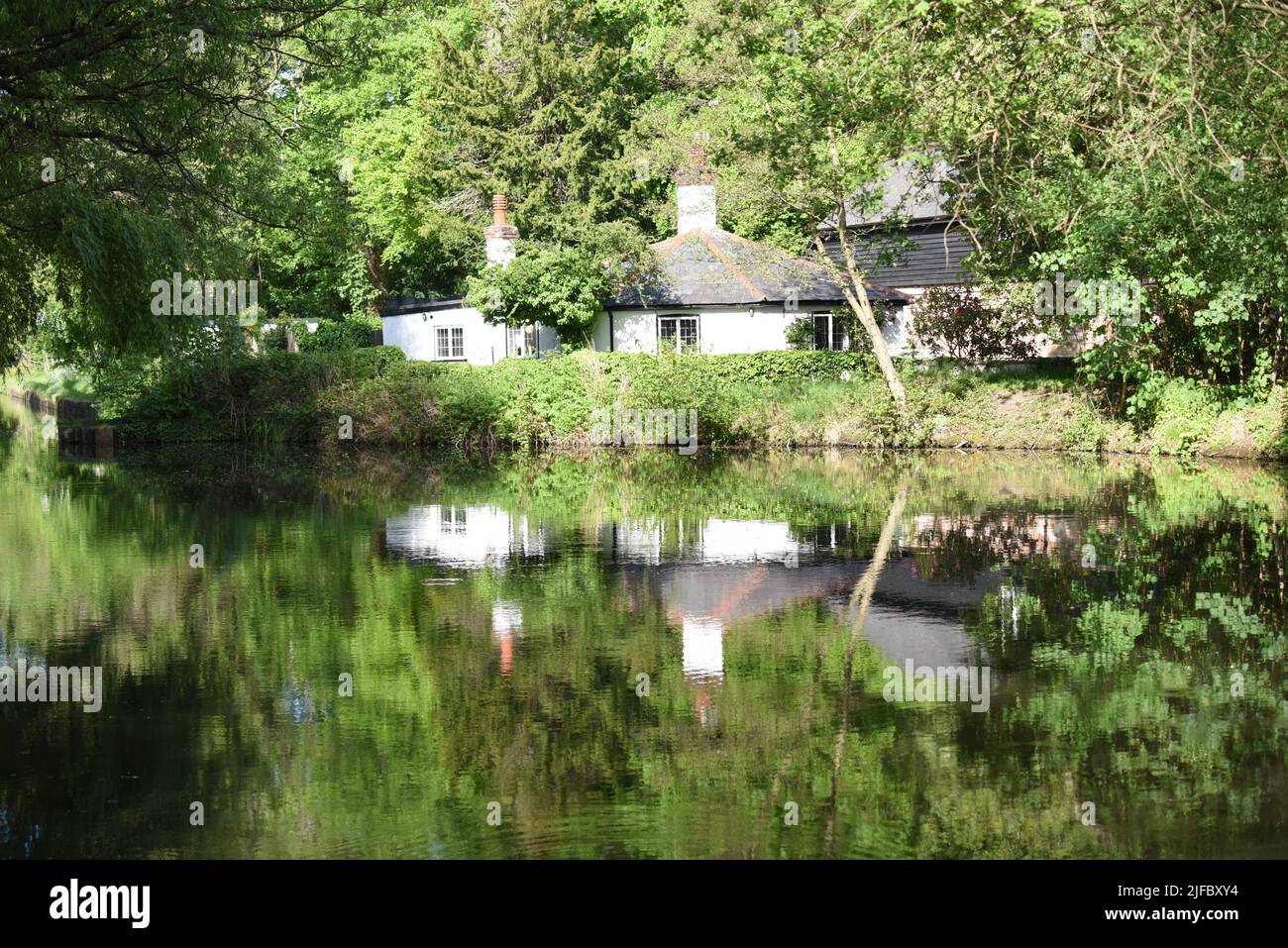 An old cottage is reflected in the still waters of the beautiful Basingstoke Canal near Frimley Green in Surrey Stock Photo