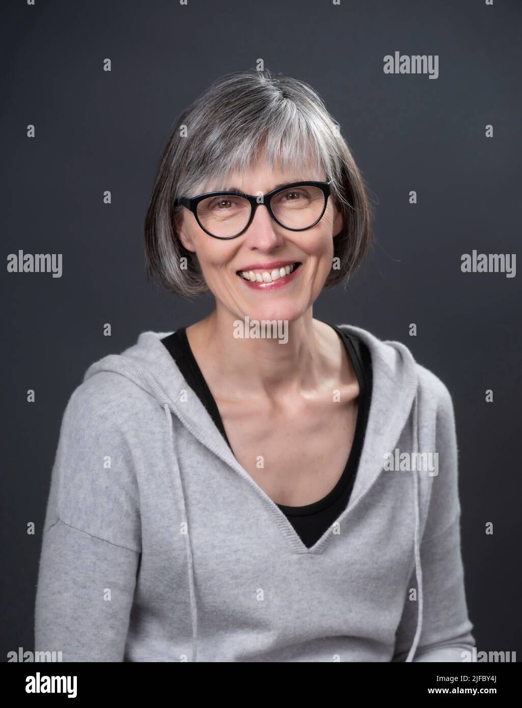 Grey-haired, middle-aged caucasian female, wearing glasses, looking at the camera, smiling. Stock Photo