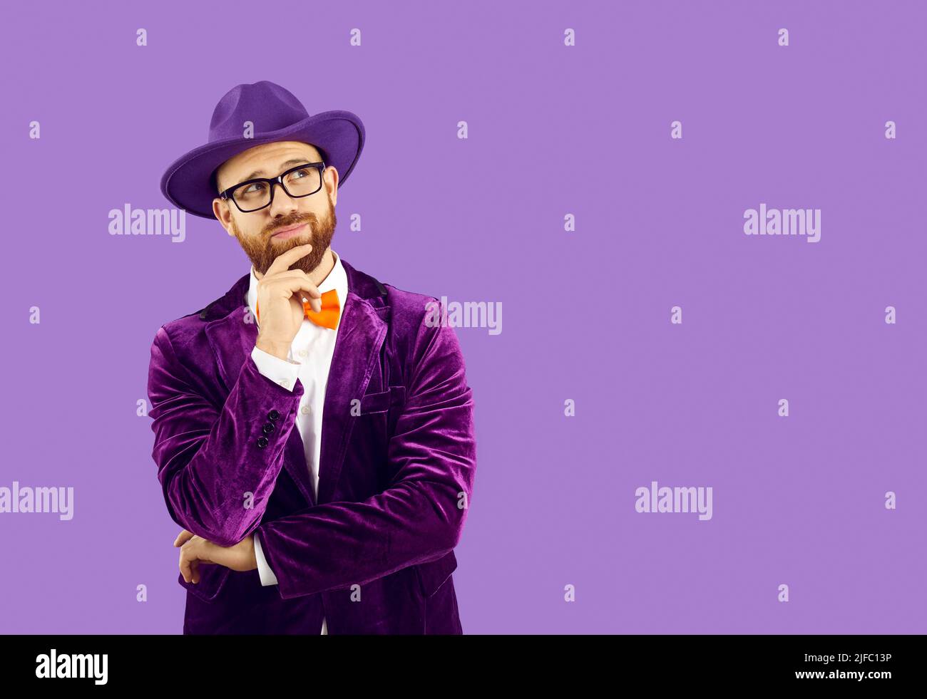 Funny curious man in hat and glasses looking at purple copy space background and thinking Stock Photo