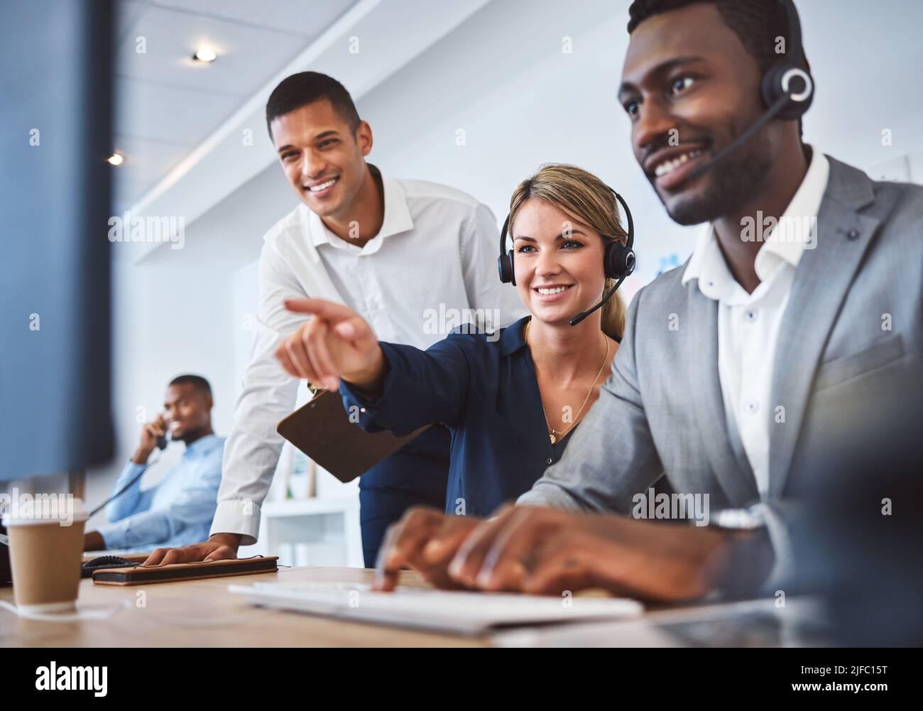 Happy caucasian female call centre telemarketing agent discussing plans with diverse colleagues while working together on computer in an office Stock Photo