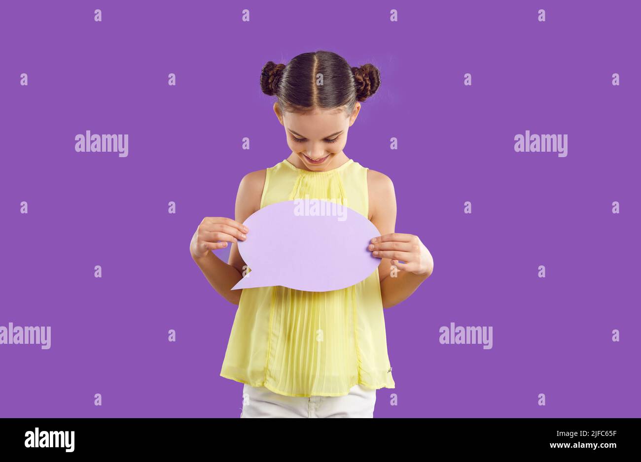 Happy smiling elementary school girl with text bubble standing on purple studio background. Stock Photo