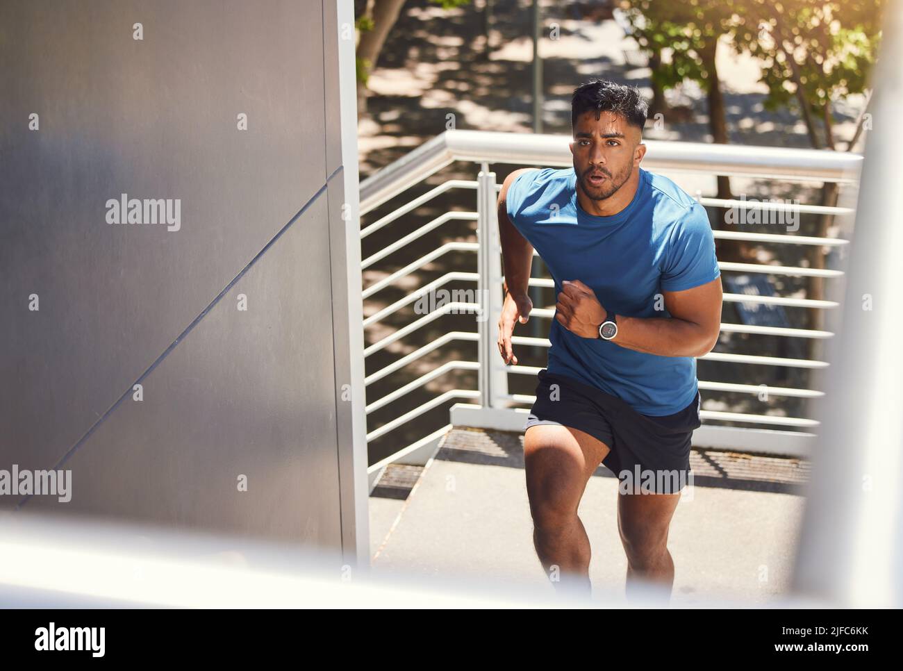 Handsome mixed race athletic man running up the steps on of a building while focused on his fitness. Hispanic male serious about his health while Stock Photo