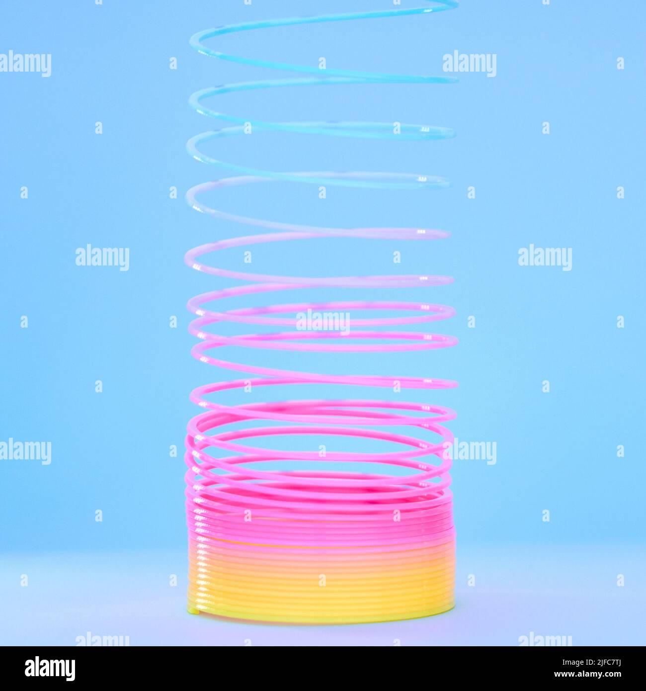 Spiral slinky toy isolated against a blue background. Closeup of a colourful retro plastic toy stretching, twirling and coiling. Spring toy for Stock Photo