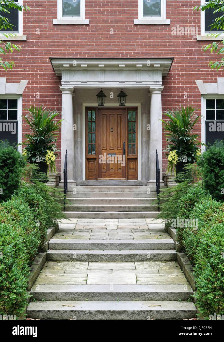 Long flagstone path leading to portico entrance of traditional brick house, with elegant wood grain front door with sidelights Stock Photo