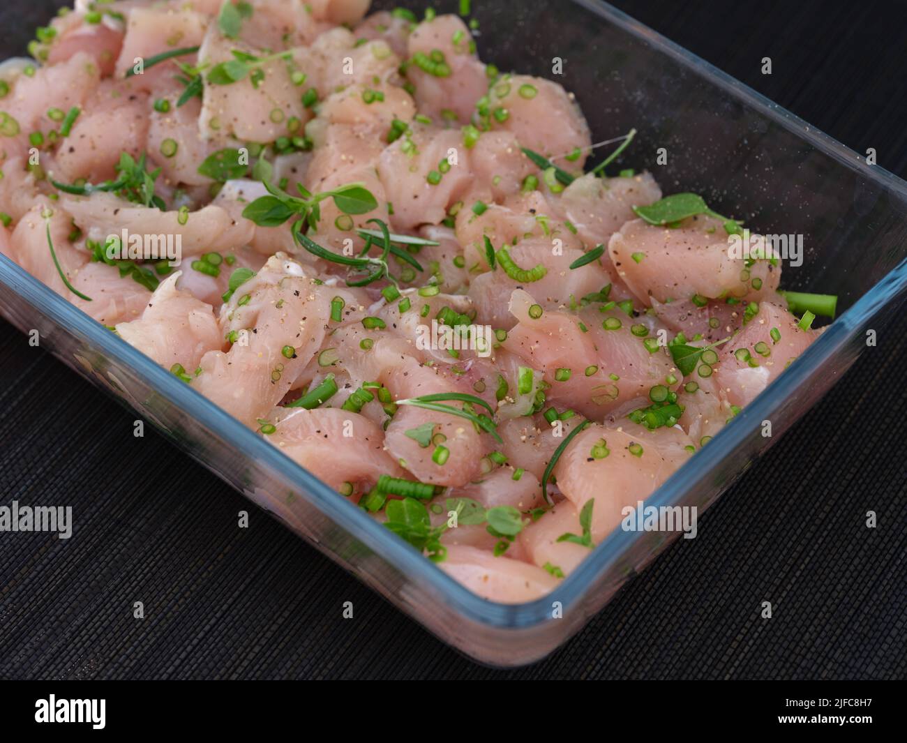 A glass baking tray with raw chicken breast with chopped garlic arrows and basil leaves. Close up. Stock Photo