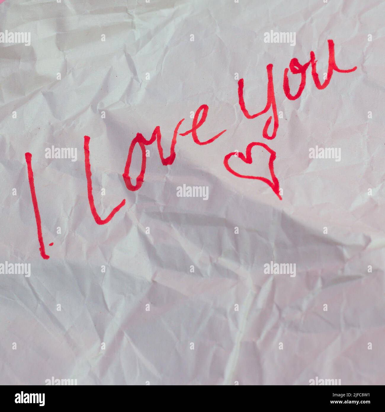 A closeup shot of a white crumpled paper with a confession saying I love you and a heart Stock Photo
