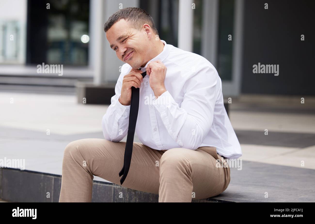 A young mixed race business man taking off his tie while sitting