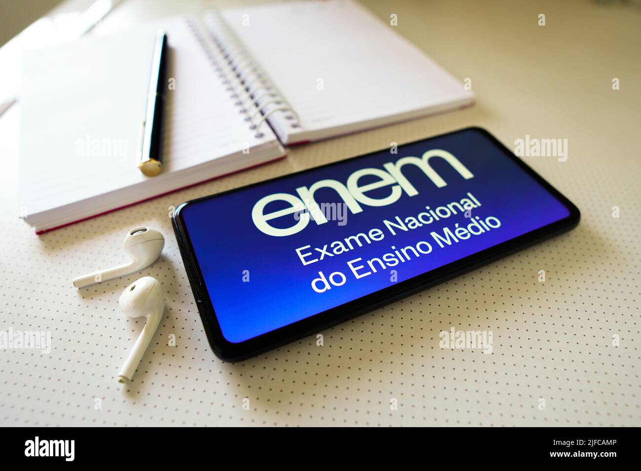 In this photo illustration the Exame Nacional do Ensino Médio (Enem) logo seen displayed on a smartphone next to a book, pen and headphones. Stock Photo