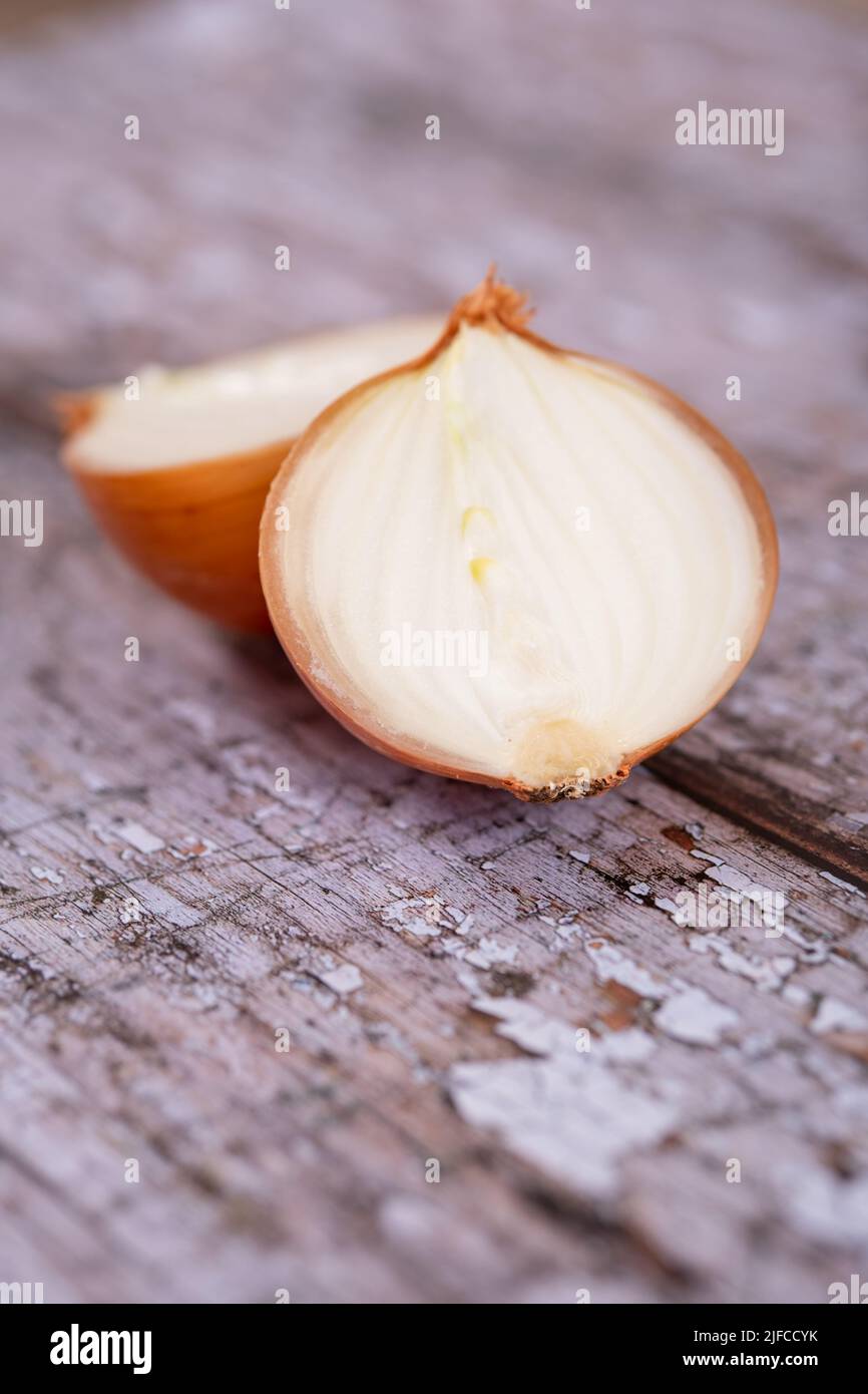 A halved white onion with skin on, against a wooden table top surface