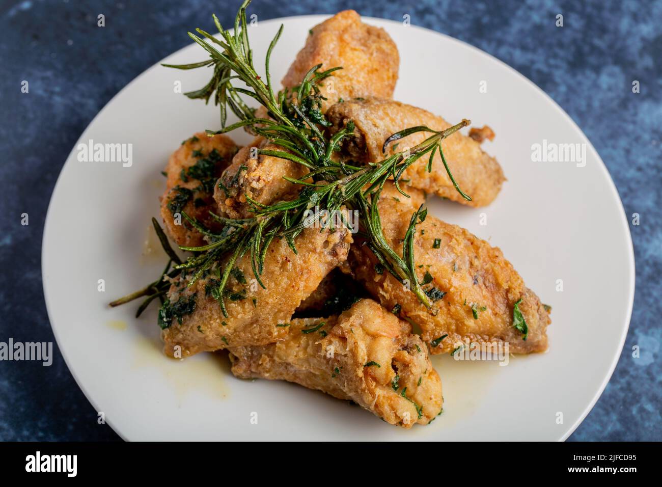 A top view of fried crispy chicken wings and rosemary leaves on a plate