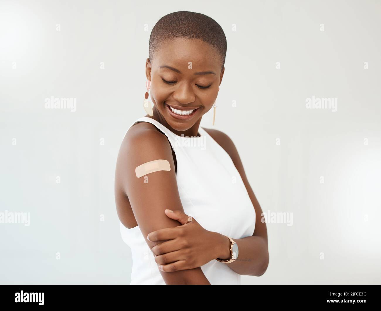 Young African American woman wearing and showing a bandaid on her arm standing against a white studio background. Happy young woman standing with a Stock Photo