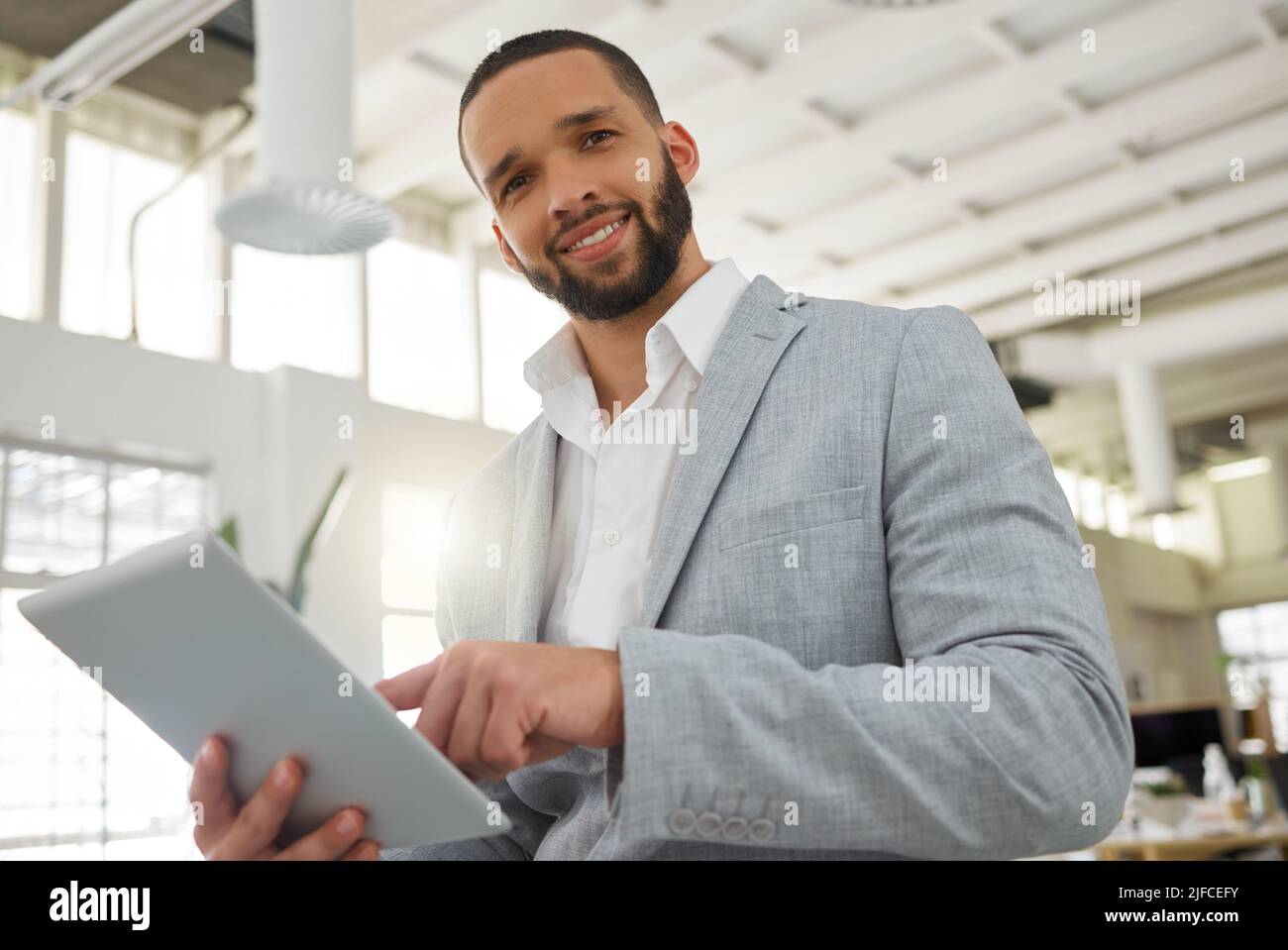 Portrait of a young happy mixed race businessman working on a digital tablet in an office. One hispanic male boss smiling and holding a digital tablet Stock Photo