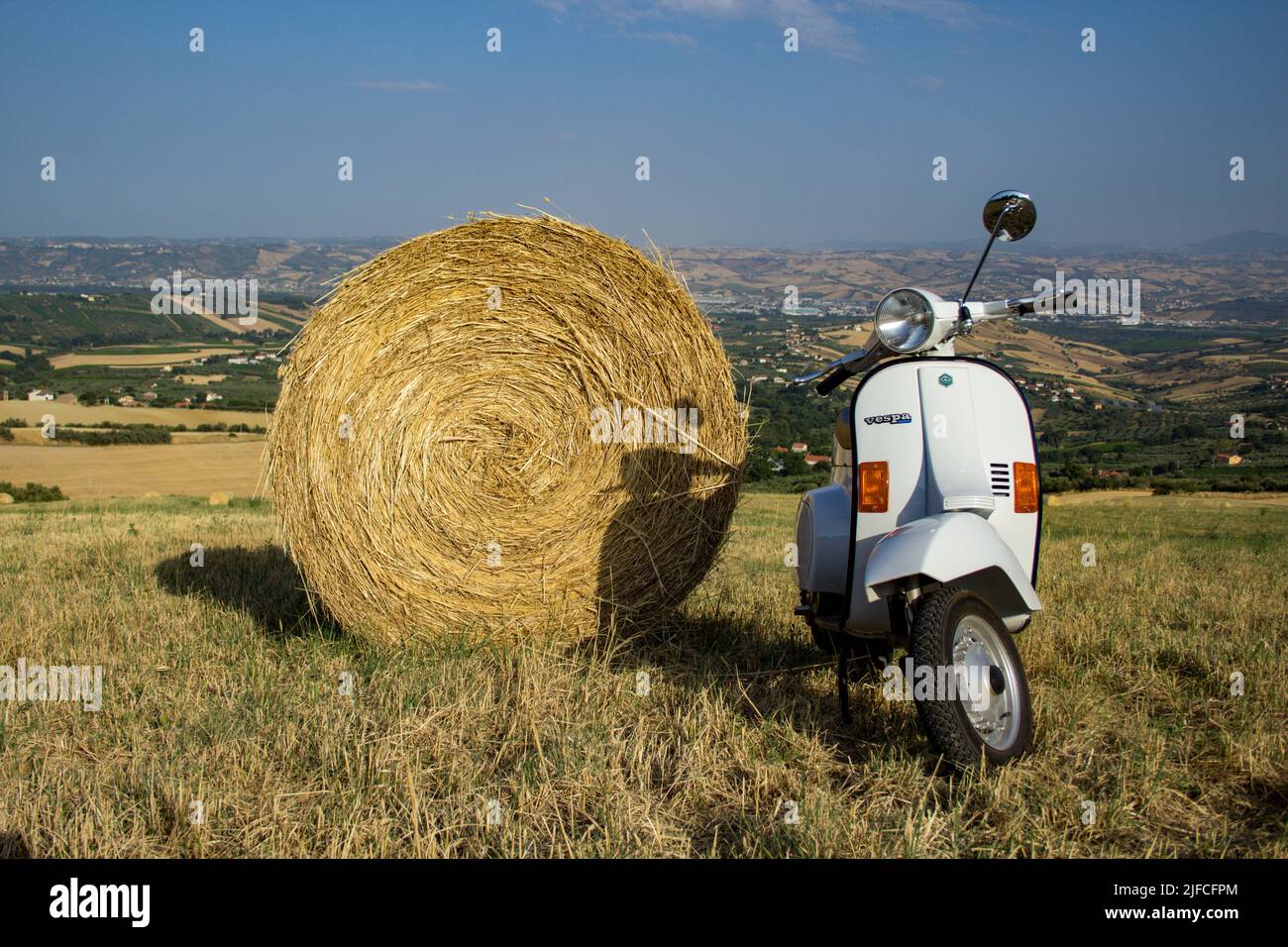 Image of an old Piaggio vespa motorcycle parked in a field with straw bales and stunning view in the background. Date 29-06-2022 Florence Italy Stock Photo
