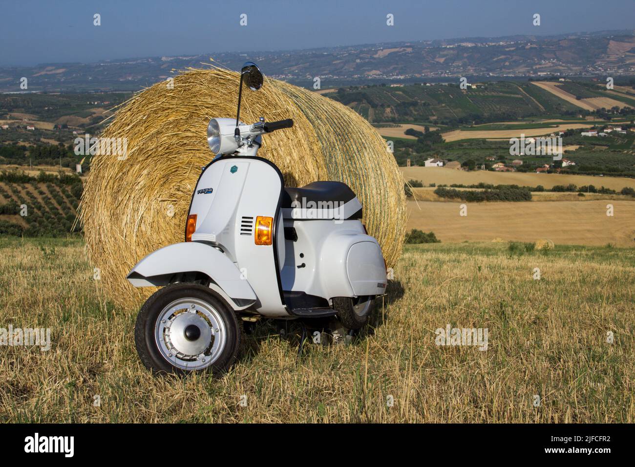 Image of an old Piaggio vespa motorcycle in a field with straw bales. Date 29-06-2022 Tuscany Florence Italy Stock Photo