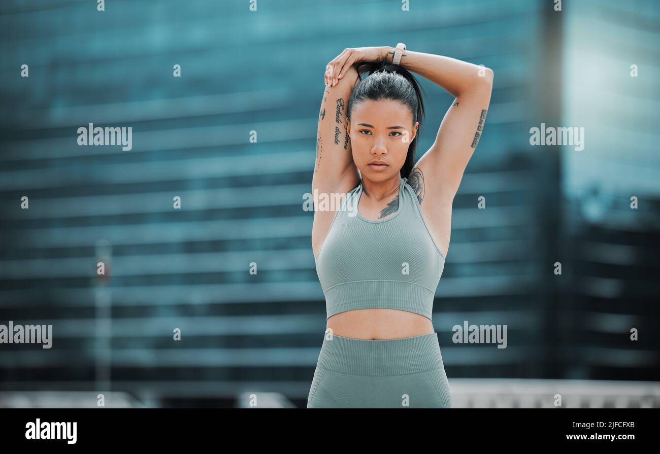 Portrait of a young hispanic female athlete looking serious while stretching before exercising outside in the city. Young woman warming up her muscles Stock Photo