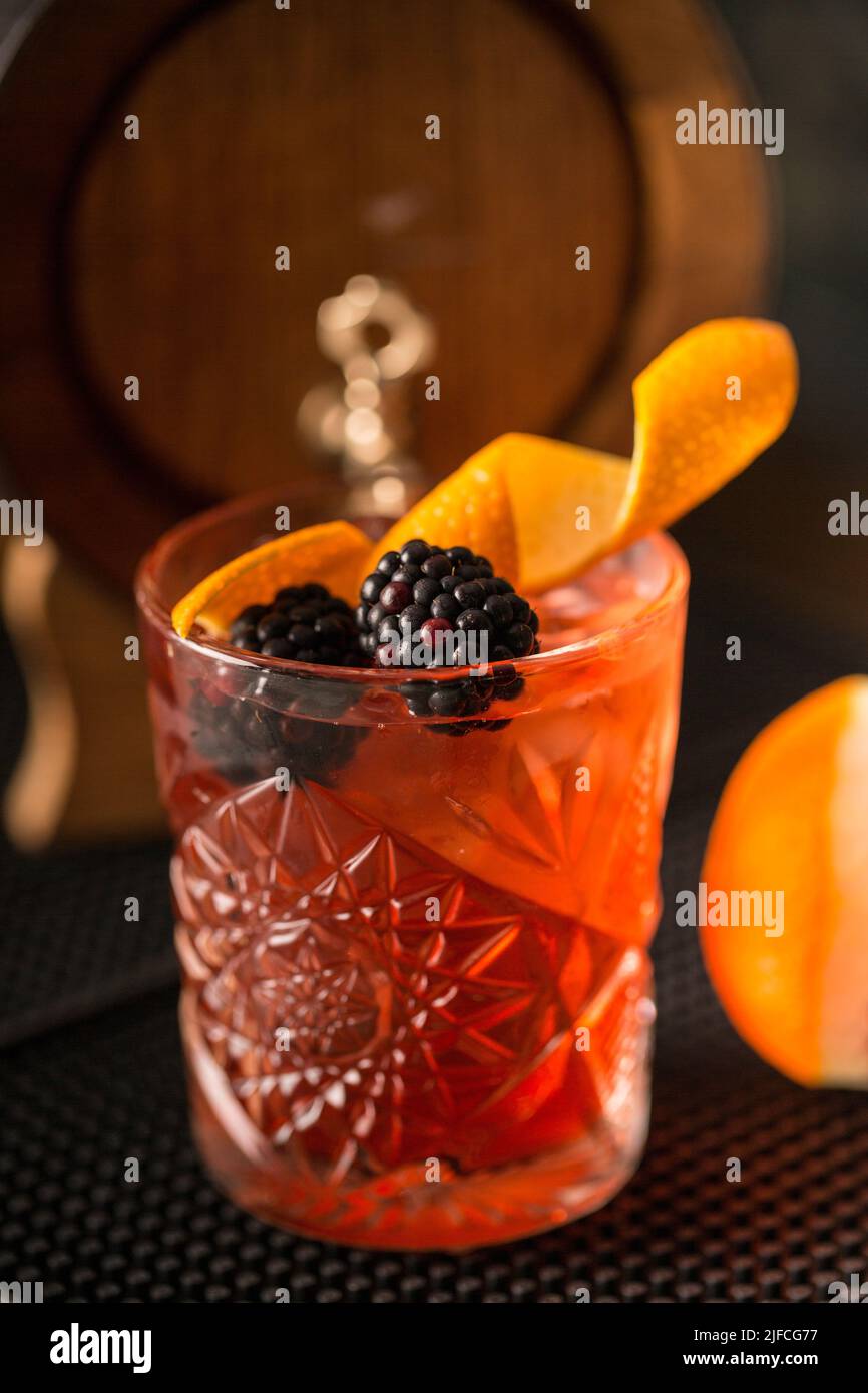 A vertical shot of a red cocktail with blackberries and orange peel on top - Black Demure Stock Photo