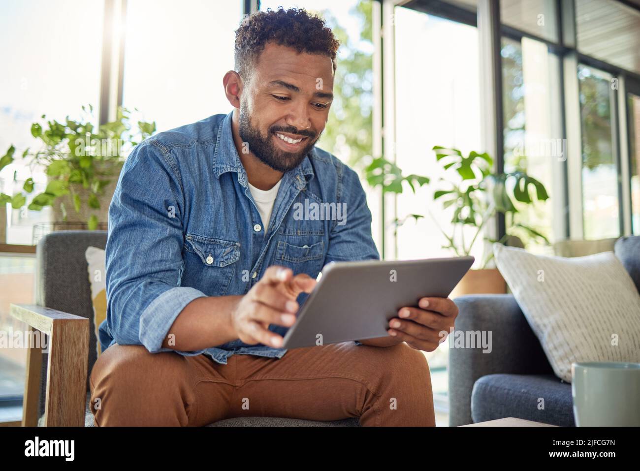 Hispanic man using his digital tablet at home. Young bachelor using his wireless device in his apartment. Handsome man browsing the internet on his Stock Photo