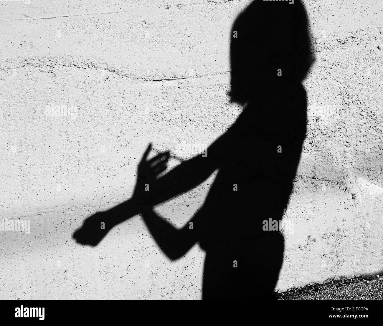Black Shadow on the wall of a drug addict boy during injection with syringe in the city suburb Stock Photo