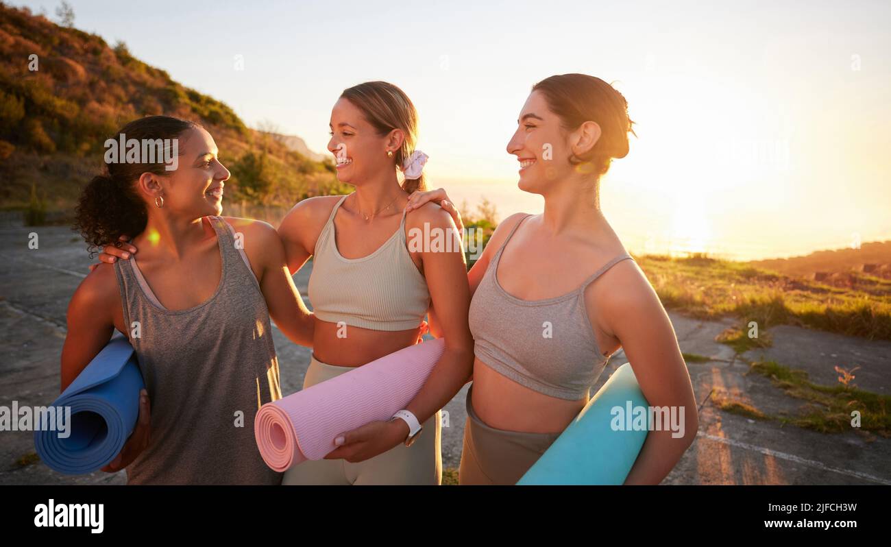 Beautiful yoga women bonding and holding yoga mats in outdoor practice in remote nature. Diverse group of young smiling active friends standing Stock Photo