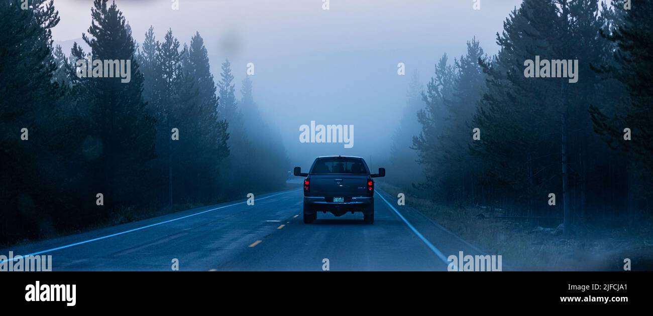 A back view of a car riding on a foggy road in Yellowstone National Park, Rigby, United States Stock Photo