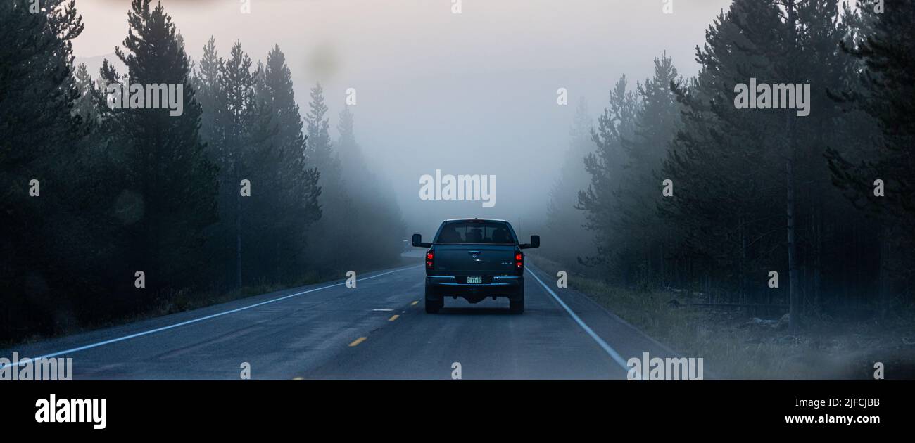 A back view of a car riding on a foggy road in Yellowstone National Park, Rigby, United States Stock Photo