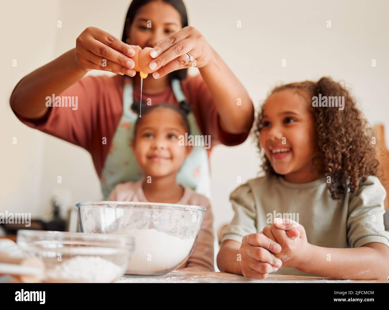 Females only, happy mixed race family of three cooking in a messy kitchen together. Loving black single parent bonding with her daughters while Stock Photo