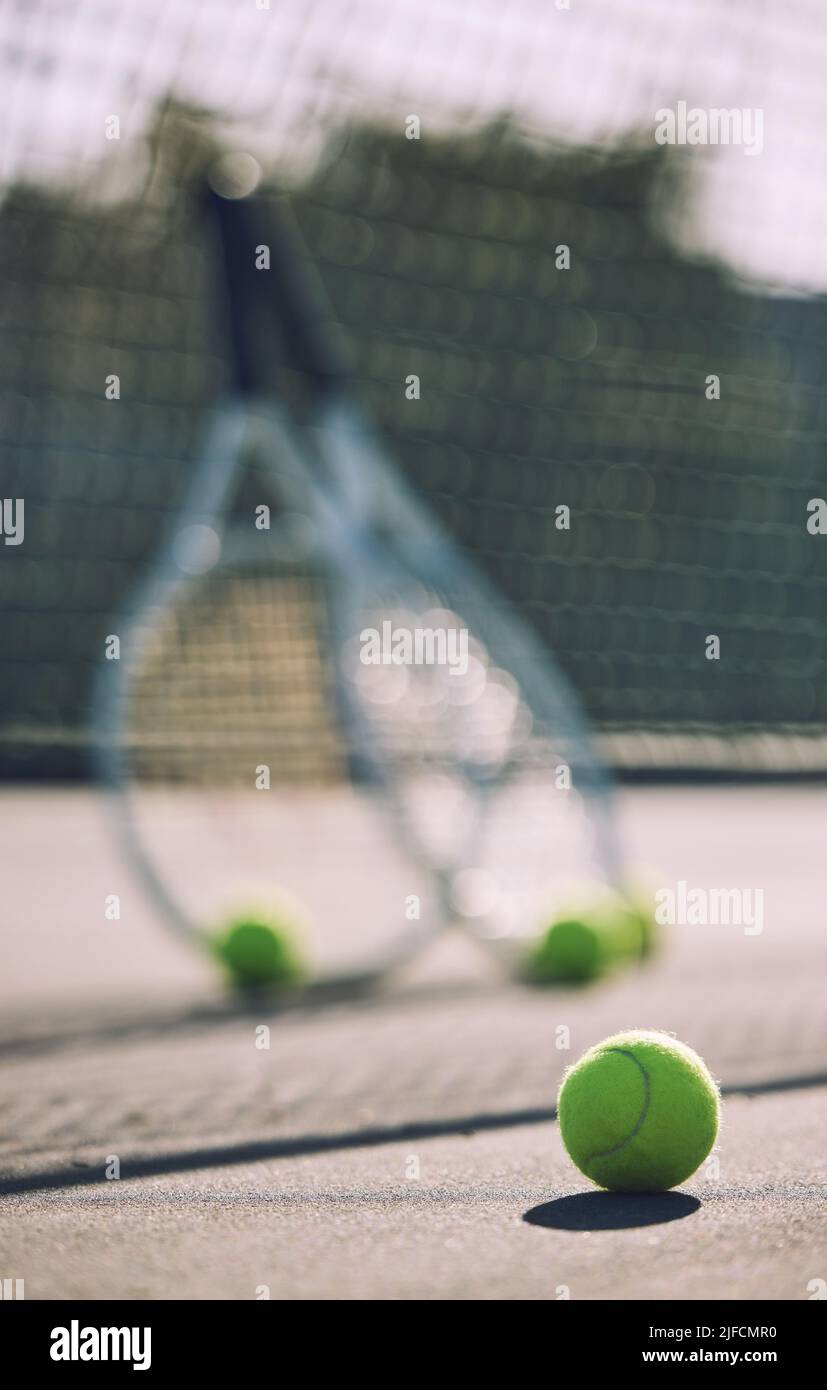 Group of tennis balls and rackets against a net on an empty court in a sports club during the day. Playing tennis is exercise, promotes health Stock Photo