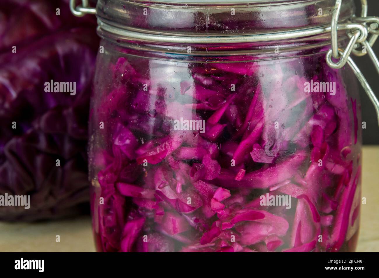 Jar of freshly made sauerkraut with whole red cabbage behind close up, macro. Stock Photo