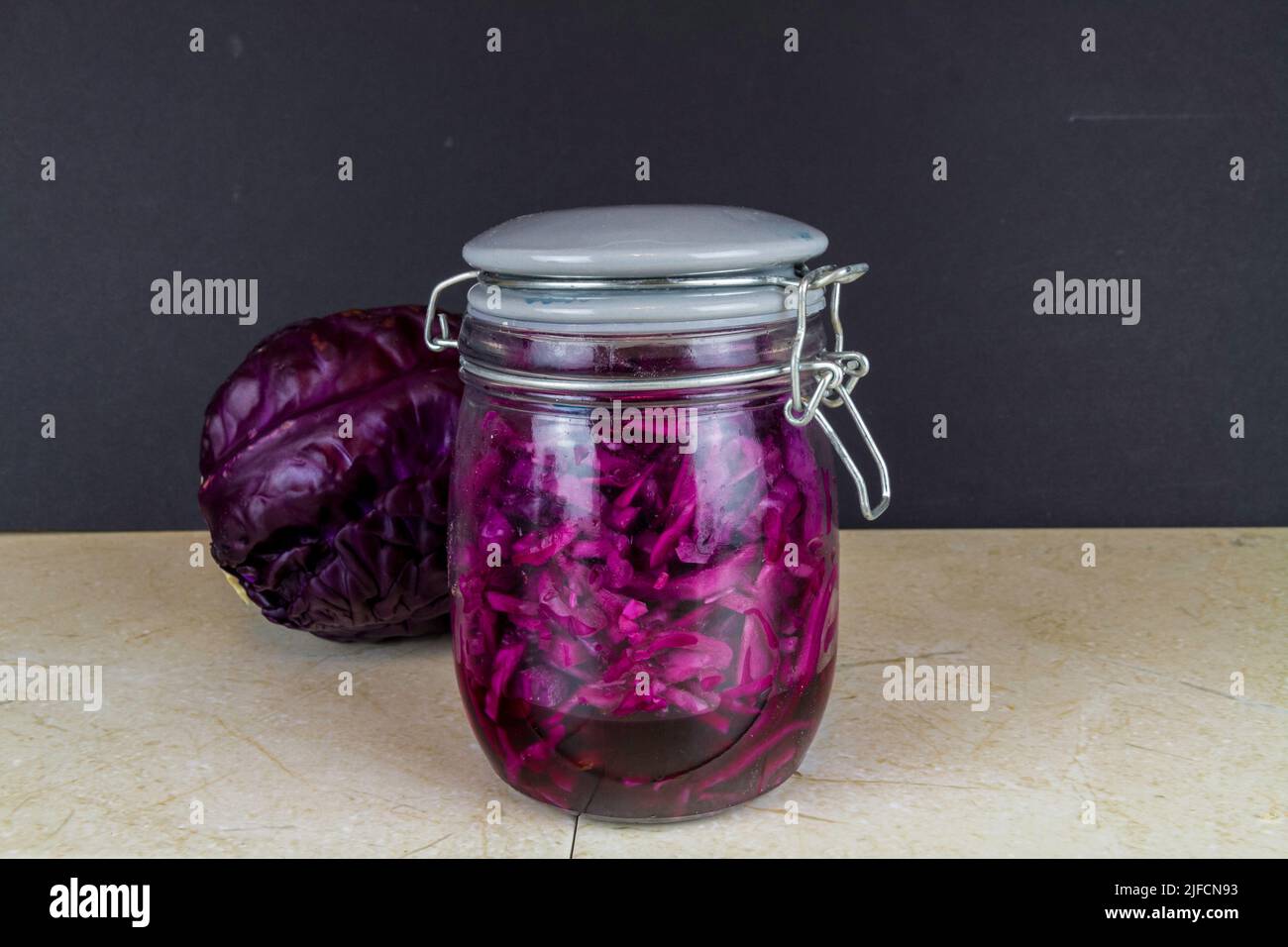 Jar of freshly made sauerkraut with whole red cabbage behind. Stock Photo