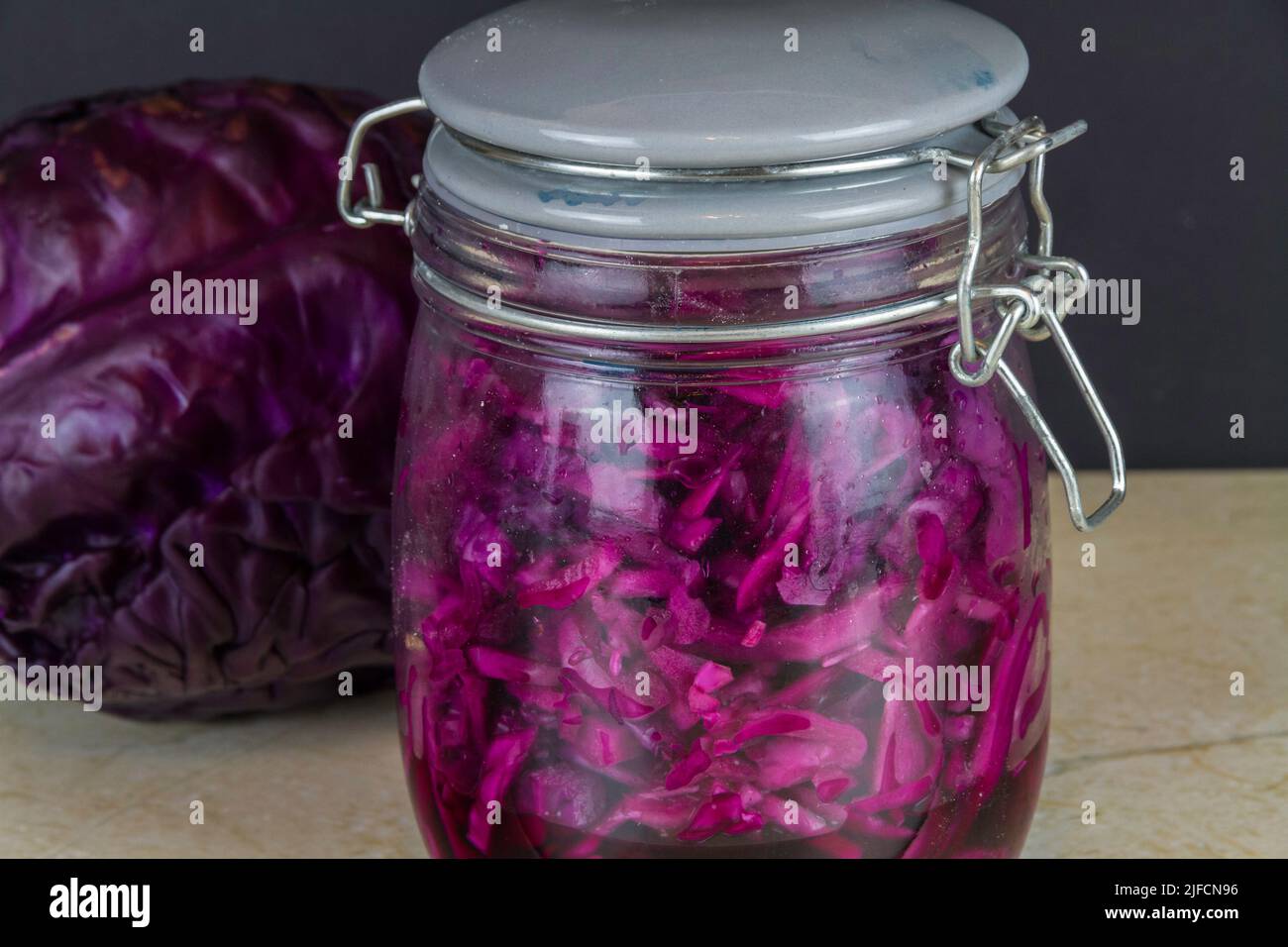 Jar of freshly made sauerkraut with whole red cabbage behind, landscape, zoomed in. Stock Photo