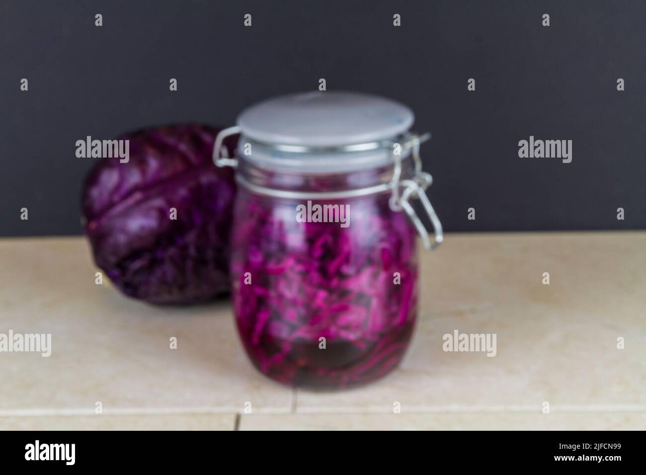 Jar of freshly made sauerkraut with whole red cabbage behind, blurred. Stock Photo